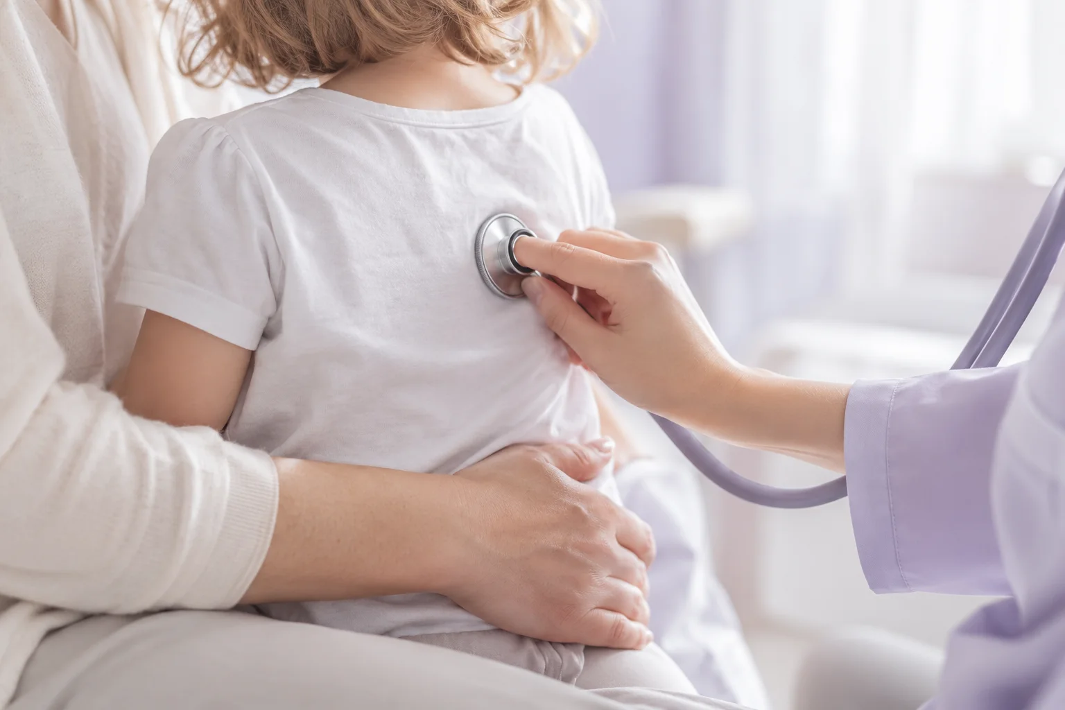 A doctor listening to a toddler with a stethoscope while the mother holds the child